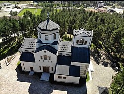 A view of the white tower and red roofs of the Orthodox church on Zlatibor through the branches of autochthonous pines that frame the picture and emphasize the natural ambience of the mountain where this shrine is located