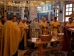 Priest Dejan Vojisavljević at the moment of performing the rite of consecration of the Slava grain and wine in front of the entrance to the Church of the Transfiguration of the Lord, surrounded by a multitude of faithful people who came to mark the temple slava
