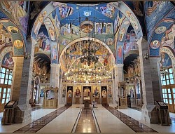 The interior of the Church of the Transfiguration in Zlatibor shows a lavish golden iconostasis with elaborately painted icons of saints, high vaults covered with vividly colored frescoes and light pouring in through the tall windows of the dome, creating a spirit of peace and prayer