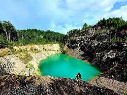 White limestone peaks jutting sharply from green mountain meadows A dense coniferous forest with tall spruce and pine trees covering the mountain slopes A view of the Čigota mountain range as clouds descend low over its peaks The crystal clear water of a mountain lake reflecting the slender pine trees on the shore Beams of sunlight breaking through the pine tree crowns on Tornik A flock of sheep scattered across the wide golden meadows at the foot of the mountain